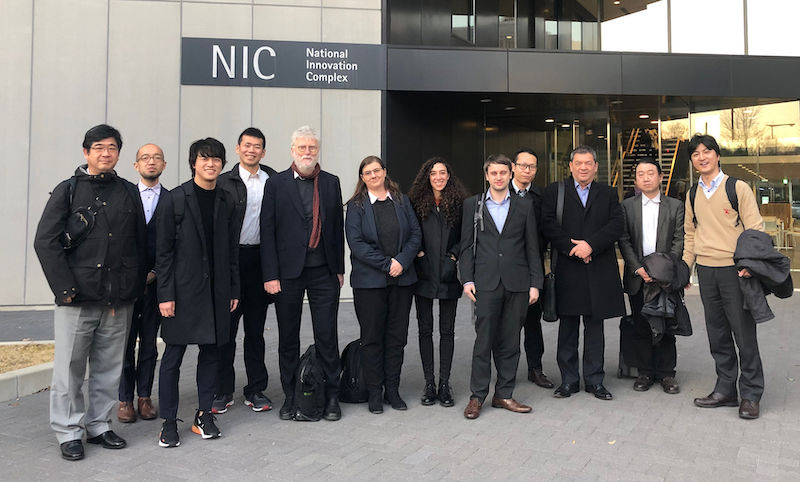 12 men and women, all members of the project team, stand in a line in front of the National Innovation Complex, Nagoya University Japan