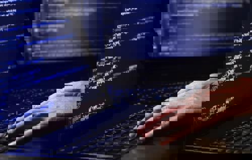 A pair of laptops both showing screens full of code. A pair of hands rests on the nearest laptop keyboard.